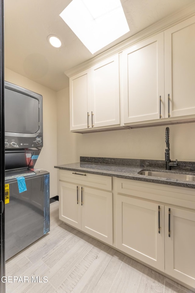 washroom with light wood-style flooring, stacked washer / dryer, cabinet space, and a sink