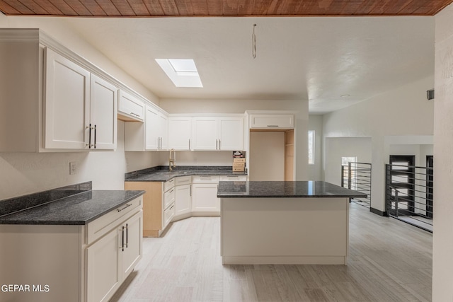 kitchen featuring light wood finished floors, a center island, dark stone counters, a skylight, and white cabinets