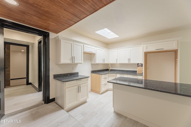 kitchen with light wood finished floors, dark stone counters, wood ceiling, a skylight, and white cabinets