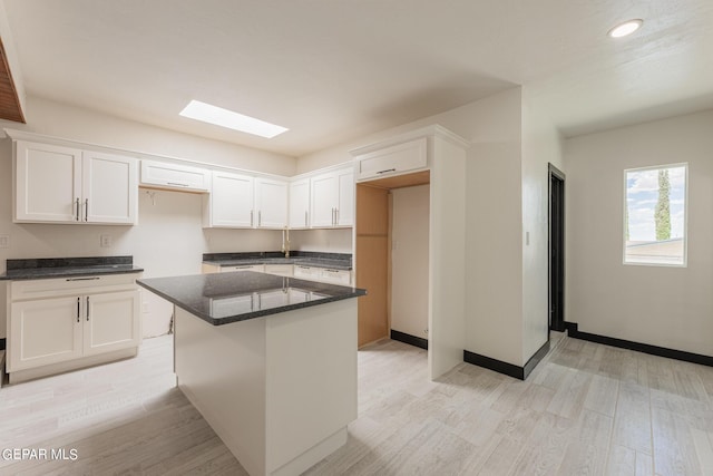 kitchen featuring baseboards, light wood-type flooring, dark stone countertops, a skylight, and white cabinets