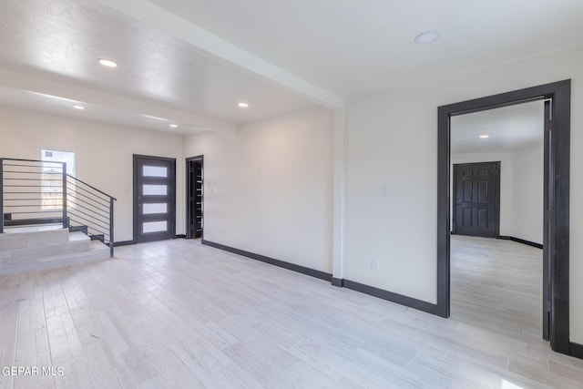 empty room featuring baseboards, beam ceiling, stairs, and light wood finished floors