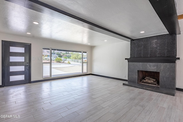 unfurnished living room with wood finished floors, baseboards, a fireplace, a textured ceiling, and beamed ceiling