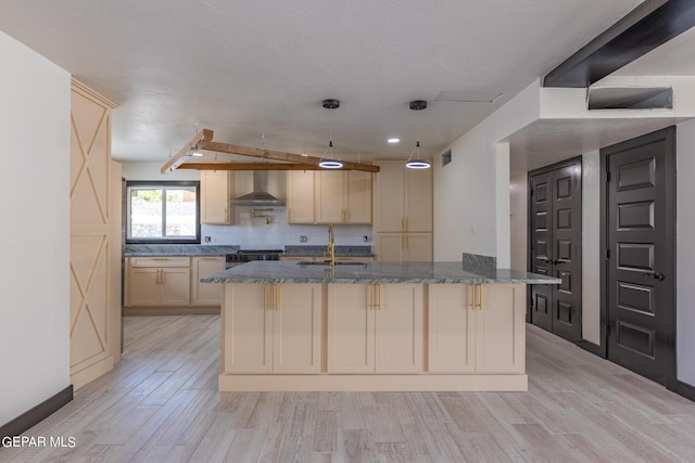 kitchen featuring dark stone counters, a sink, wall chimney exhaust hood, light wood-type flooring, and backsplash