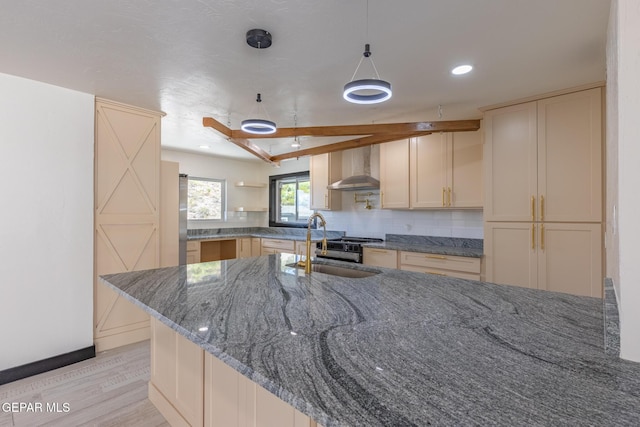 kitchen featuring backsplash, wall chimney range hood, dark stone counters, light wood-style floors, and a sink