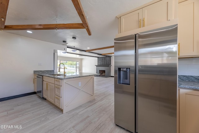 kitchen with light wood finished floors, beam ceiling, a sink, appliances with stainless steel finishes, and a brick fireplace