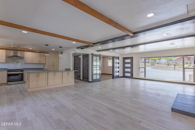 kitchen with light wood-type flooring, beam ceiling, open floor plan, a barn door, and stainless steel stove