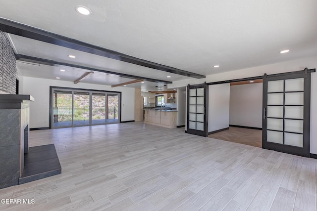 unfurnished living room with beamed ceiling, recessed lighting, light wood-style floors, and a barn door