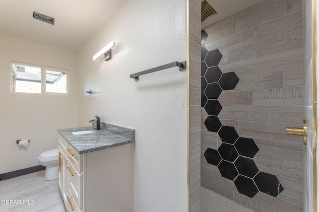 bathroom with a tile shower, toilet, vanity, and baseboards