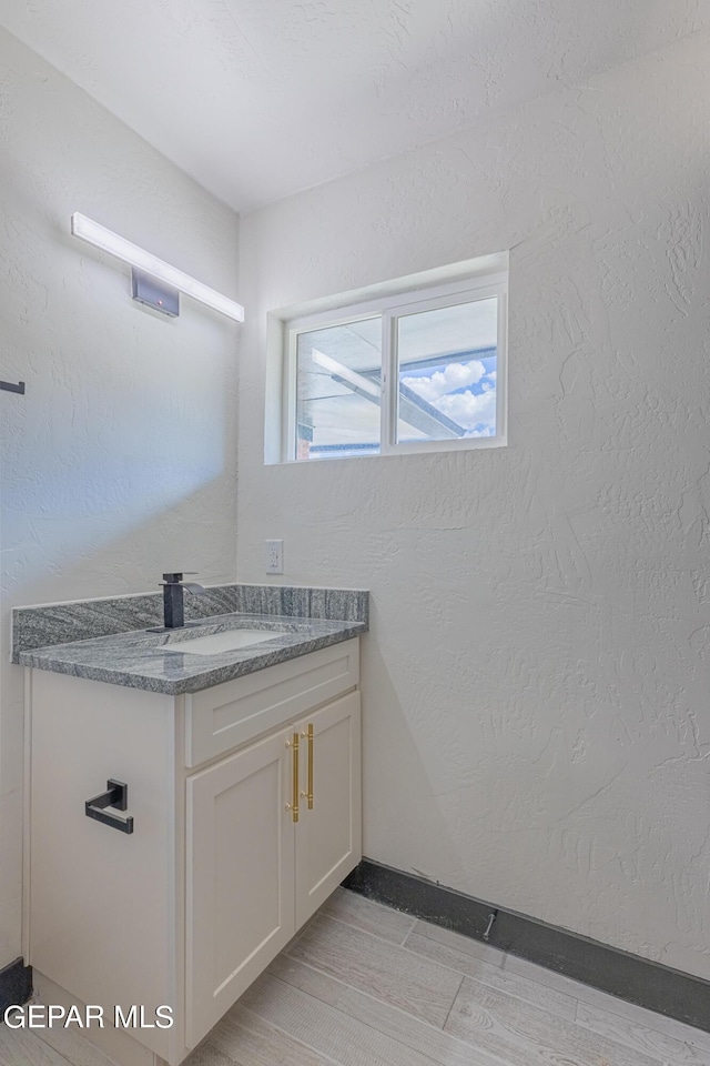 bathroom with wood finished floors, vanity, and a textured wall