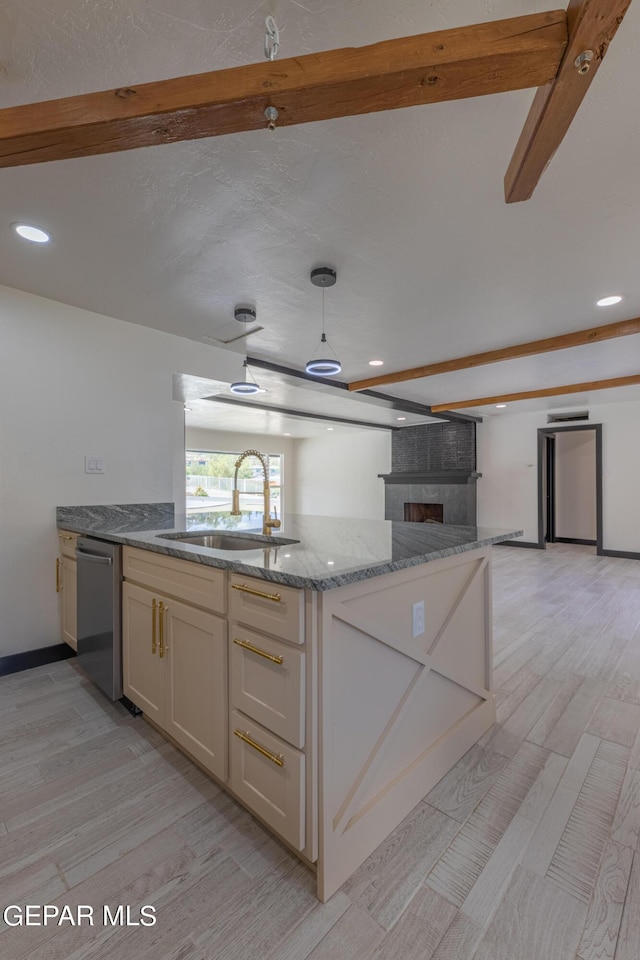 kitchen with light wood finished floors, a sink, open floor plan, stone countertops, and stainless steel dishwasher