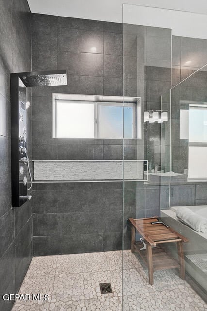 bathroom featuring tile patterned flooring, plenty of natural light, a shower with shower door, and tile walls