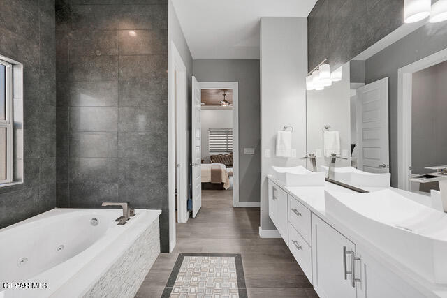 bathroom with dual vanity, wood-type flooring, and tiled tub