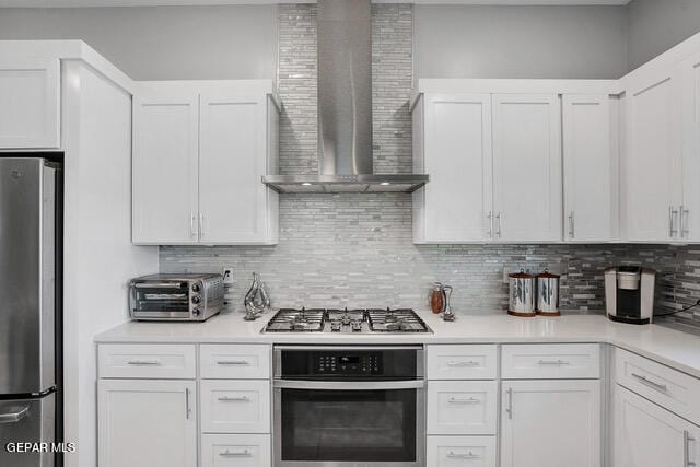 kitchen with wall chimney exhaust hood, decorative backsplash, white cabinetry, and stainless steel appliances