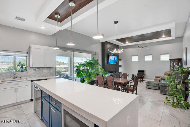 kitchen with sink, white cabinetry, a tray ceiling, ceiling fan, and hanging light fixtures