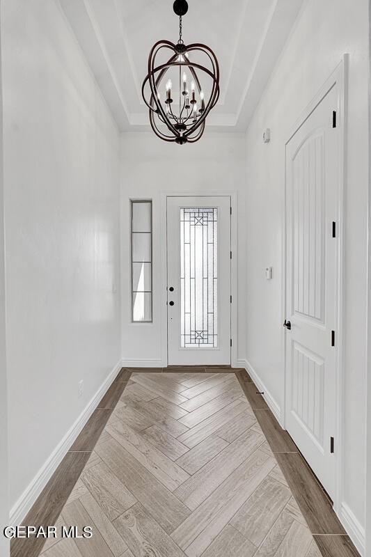 foyer entrance with a raised ceiling, a chandelier, and dark parquet floors