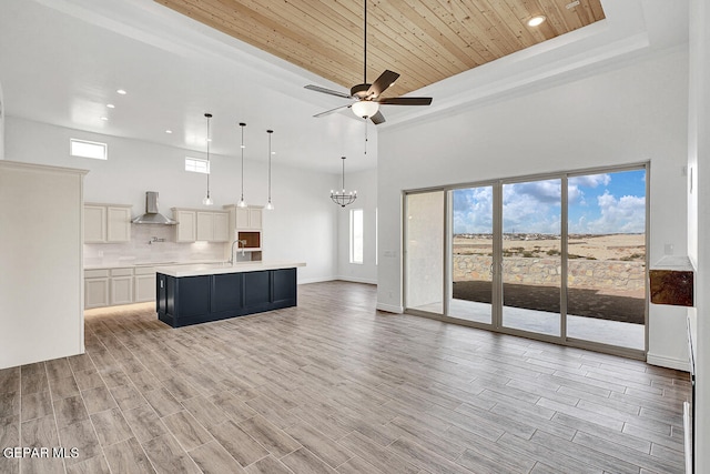 kitchen featuring wooden ceiling, a towering ceiling, an island with sink, and exhaust hood