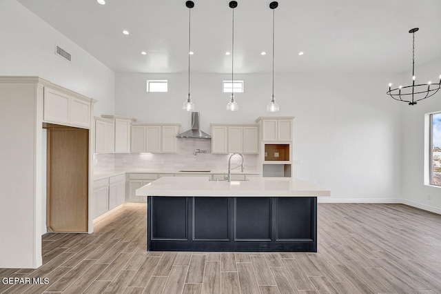 kitchen with decorative light fixtures, light hardwood / wood-style floors, wall chimney exhaust hood, and tasteful backsplash