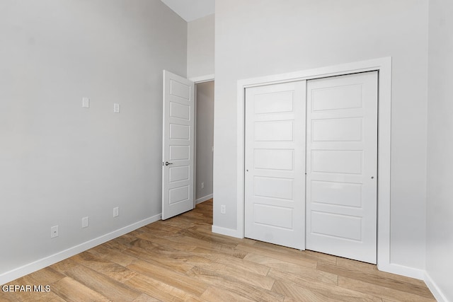 unfurnished bedroom featuring light hardwood / wood-style floors, a towering ceiling, and a closet