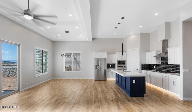 kitchen with white cabinets, decorative light fixtures, appliances with stainless steel finishes, and an island with sink