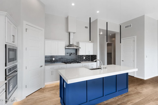 kitchen featuring appliances with stainless steel finishes, light hardwood / wood-style floors, white cabinetry, sink, and wall chimney range hood