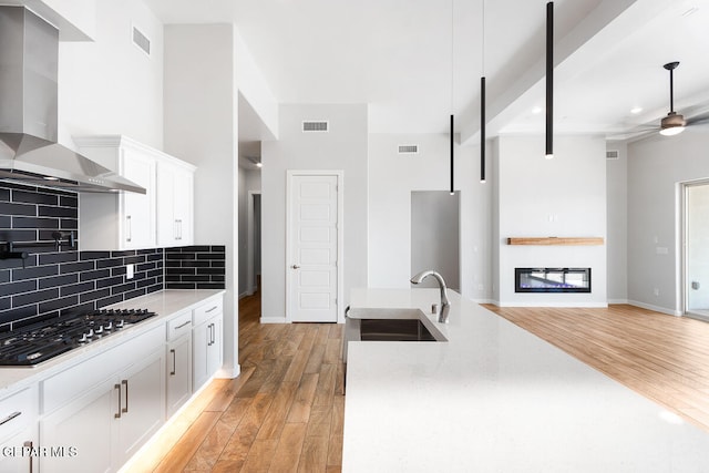 kitchen featuring wall chimney range hood, decorative backsplash, ceiling fan, black gas cooktop, and light hardwood / wood-style floors