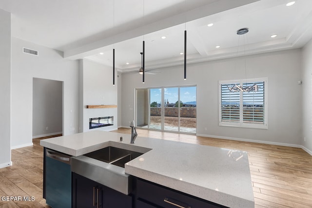 kitchen with light stone countertops, an island with sink, light hardwood / wood-style floors, dishwasher, and ceiling fan