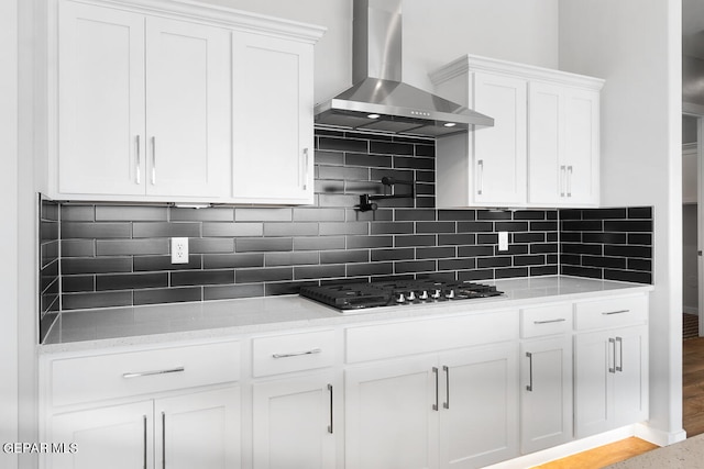 kitchen with wall chimney exhaust hood, decorative backsplash, and white cabinets