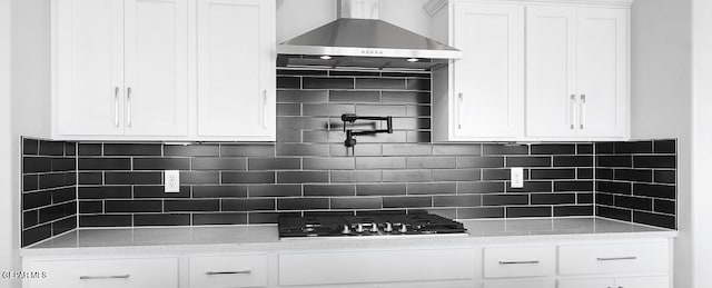 kitchen featuring wall chimney exhaust hood, backsplash, white cabinetry, and light stone counters