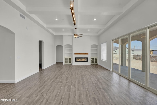 unfurnished living room with built in shelves, ceiling fan, light hardwood / wood-style floors, and beam ceiling