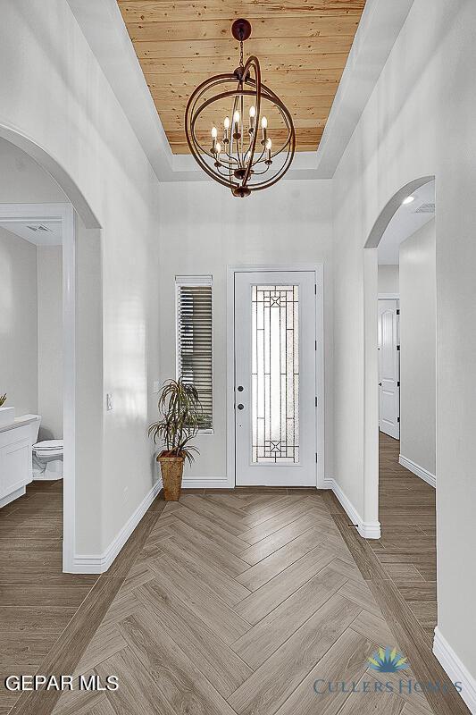 entryway with wood ceiling, a tray ceiling, a notable chandelier, and parquet floors