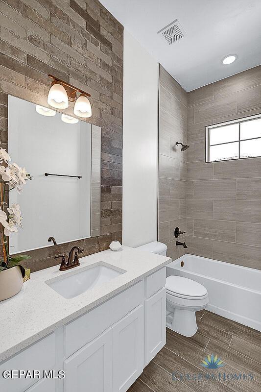 full bathroom featuring tiled shower / bath combo, brick wall, toilet, and vanity