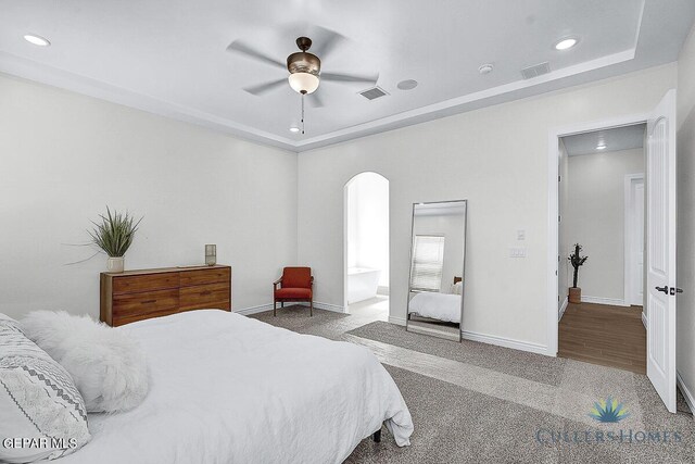 bedroom featuring ceiling fan, hardwood / wood-style flooring, connected bathroom, and a tray ceiling