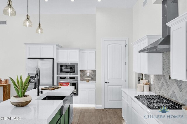 kitchen with wall chimney range hood, light wood-type flooring, backsplash, appliances with stainless steel finishes, and white cabinetry