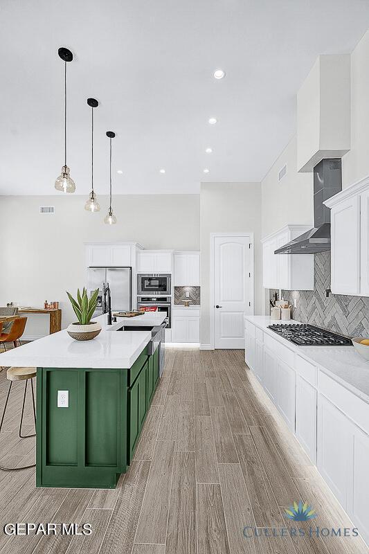 kitchen featuring appliances with stainless steel finishes, backsplash, white cabinetry, a center island with sink, and green cabinets