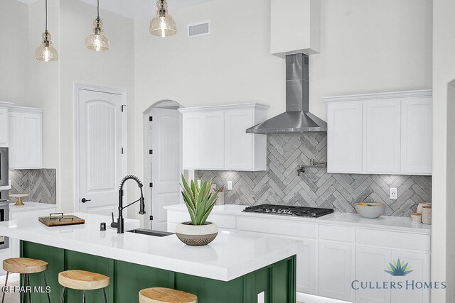 kitchen with a kitchen island with sink, tasteful backsplash, wall chimney range hood, and white cabinets