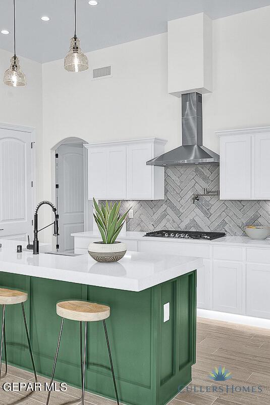 kitchen featuring backsplash, light hardwood / wood-style floors, white cabinetry, pendant lighting, and wall chimney range hood