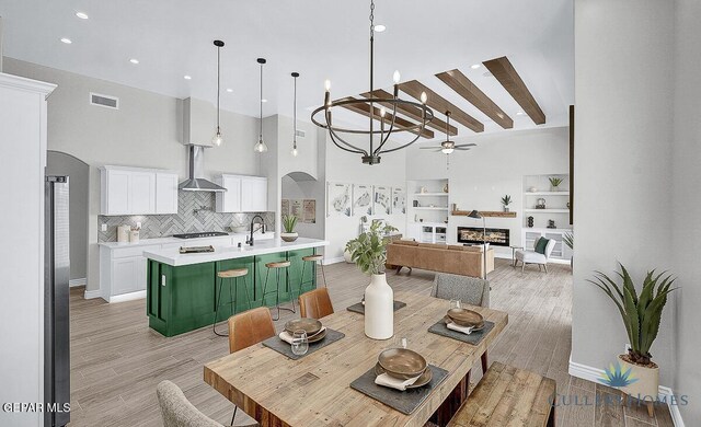 dining room featuring a towering ceiling, built in shelves, ceiling fan with notable chandelier, and light hardwood / wood-style floors