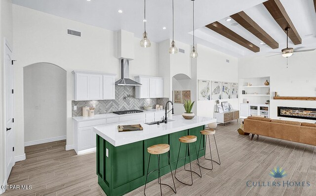 kitchen featuring wall chimney range hood, ceiling fan, light hardwood / wood-style flooring, a high ceiling, and white cabinetry