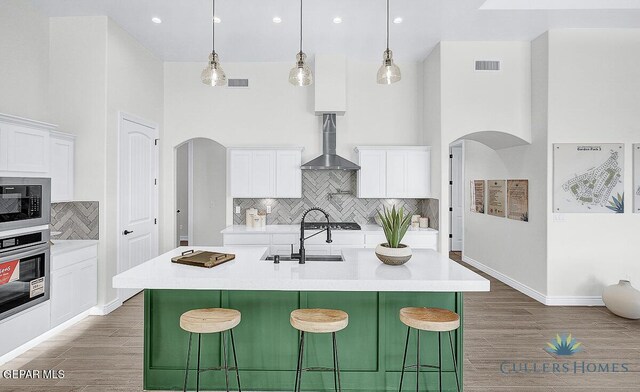 kitchen featuring backsplash, a kitchen island with sink, wall chimney range hood, wood-type flooring, and stainless steel oven