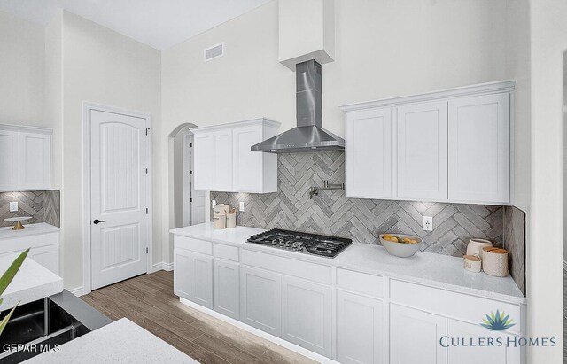 kitchen with wall chimney exhaust hood, tasteful backsplash, wood-type flooring, stainless steel gas stovetop, and white cabinetry