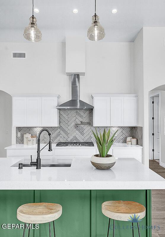 kitchen with wall chimney exhaust hood, white cabinets, and backsplash