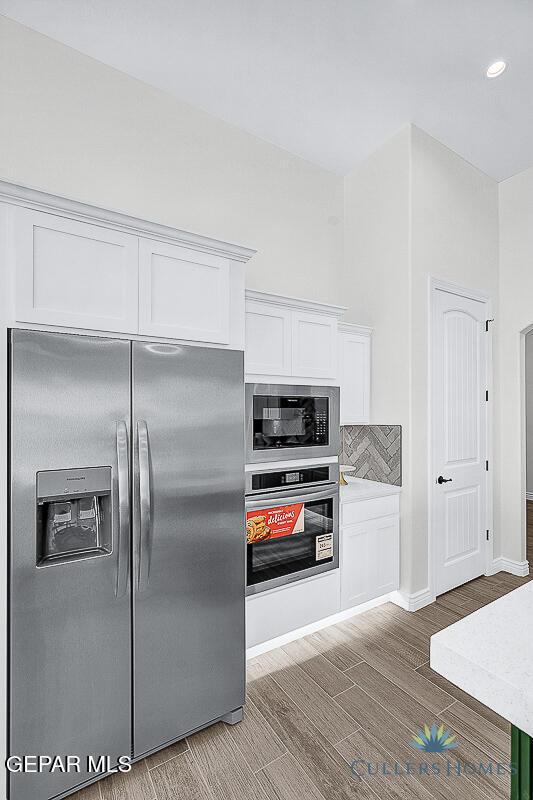 kitchen with appliances with stainless steel finishes, wood-type flooring, backsplash, and white cabinets