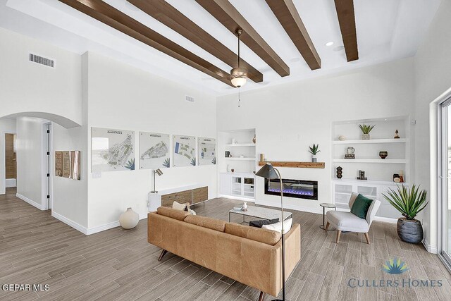 living room featuring ceiling fan, beam ceiling, hardwood / wood-style flooring, and a towering ceiling