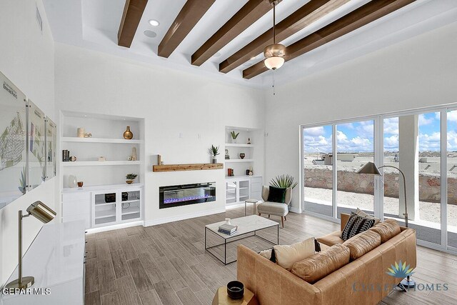 living room with hardwood / wood-style flooring, beamed ceiling, a high ceiling, and ceiling fan