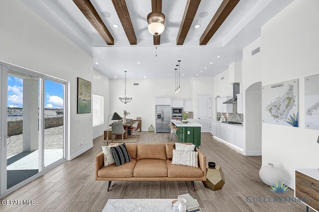 living room with ceiling fan, beam ceiling, a towering ceiling, and light hardwood / wood-style flooring