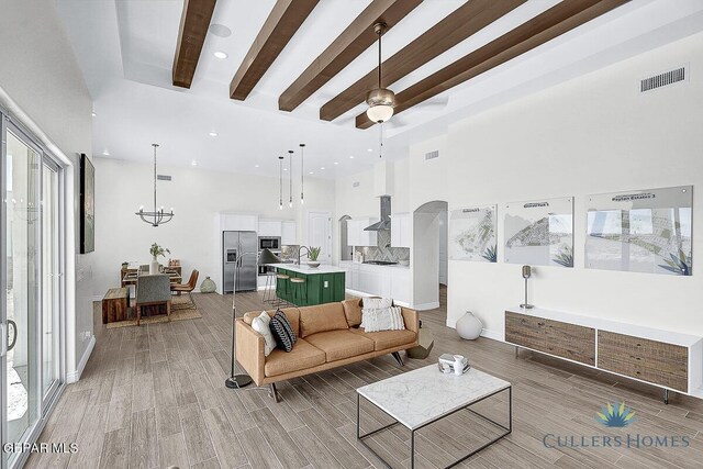 living room featuring a high ceiling, sink, beamed ceiling, light wood-type flooring, and ceiling fan with notable chandelier