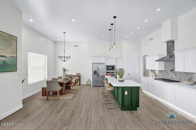 kitchen featuring stainless steel appliances, decorative backsplash, wall chimney exhaust hood, white cabinets, and a kitchen island