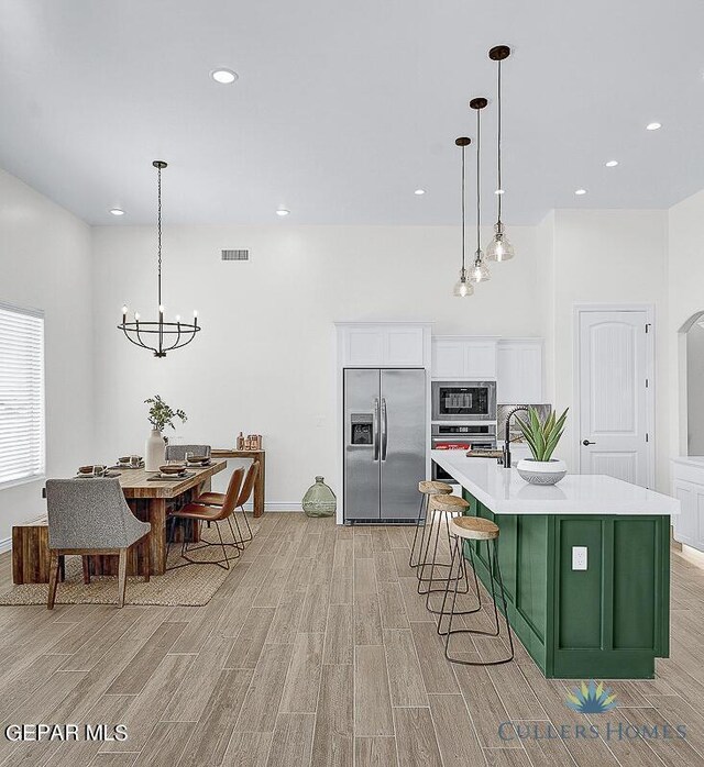 kitchen featuring hanging light fixtures, light hardwood / wood-style floors, a kitchen island with sink, white cabinetry, and stainless steel appliances