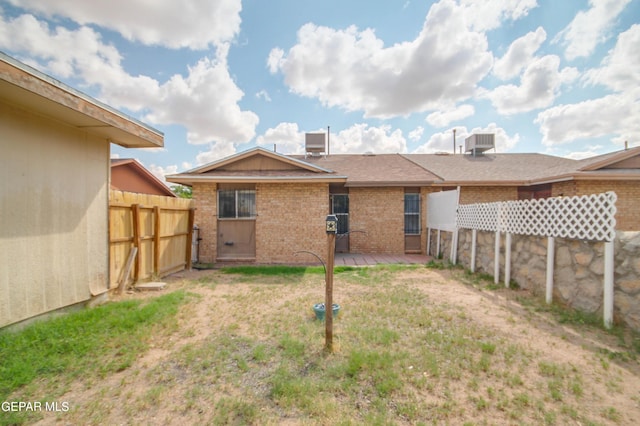 back of property with cooling unit, fence, brick siding, and a lawn