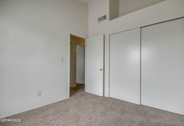 unfurnished bedroom with a closet, a towering ceiling, visible vents, and carpet floors